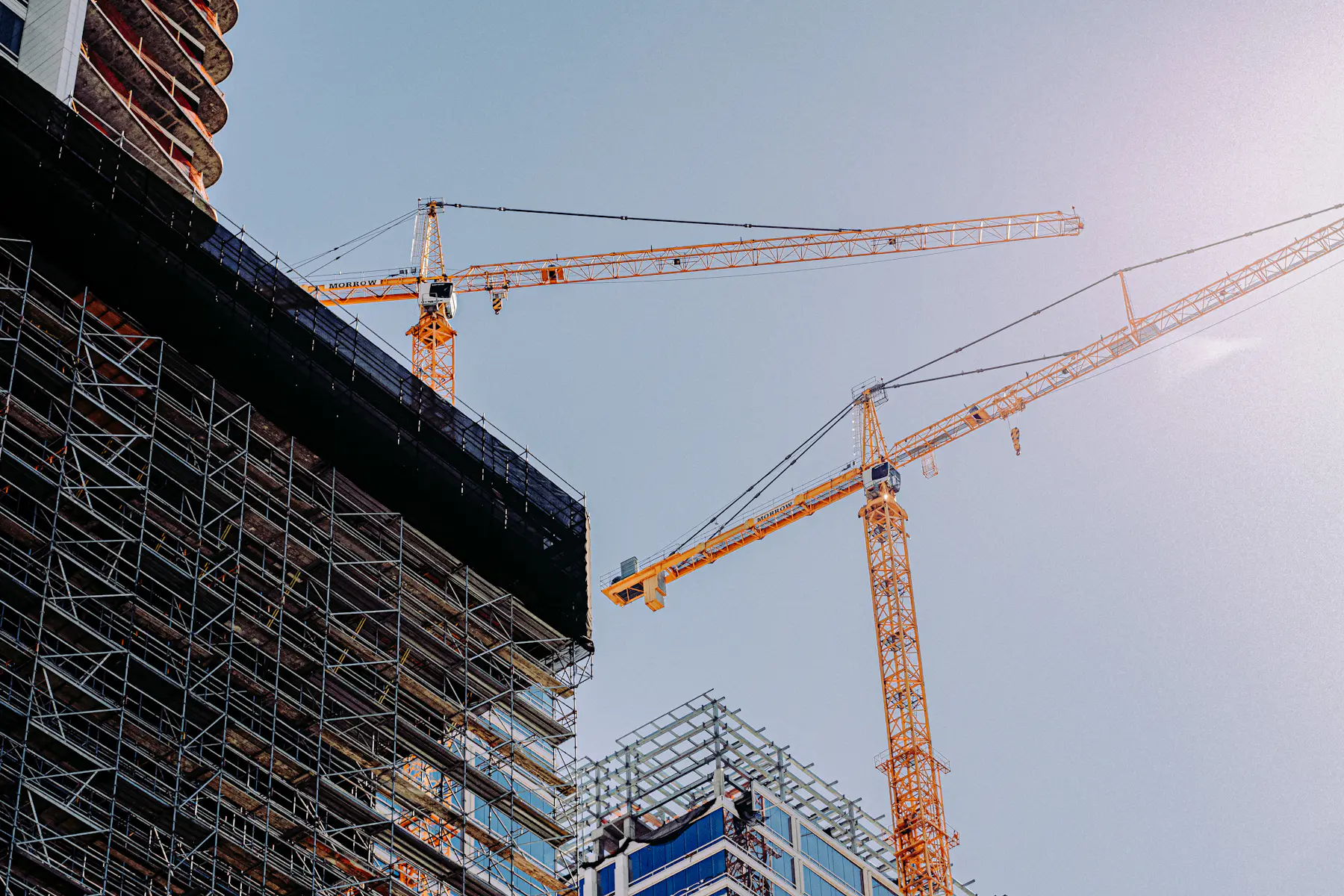 Zwei Rohbauten mit eigenem Turmdrehkran und Gerüst als Hintergrund der Seite zur Projektsteuerung in Bau und Infrastruktur.